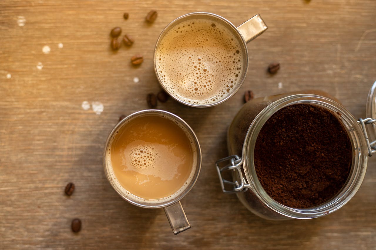 Aerial shot of coffee cups and ground coffee in a jar on a wooden surface, creating a cozy atmosphere.
